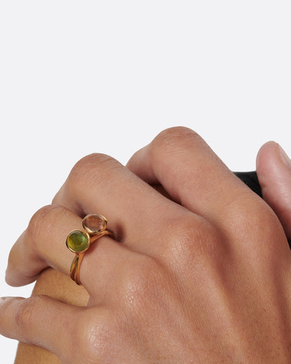 A yellow gold ring with a green tourmaline cabochon, shown stacked with a second ring on a hand.