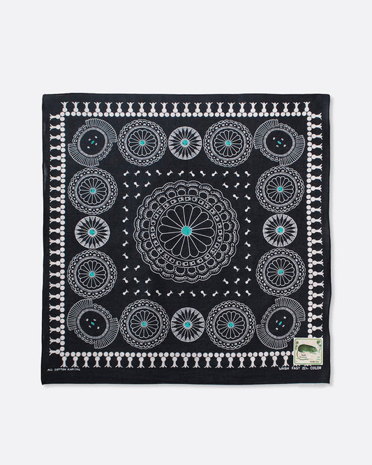 A black selvedge bandana with a pattern of turquoise- centered conchos. Shown lying flat.