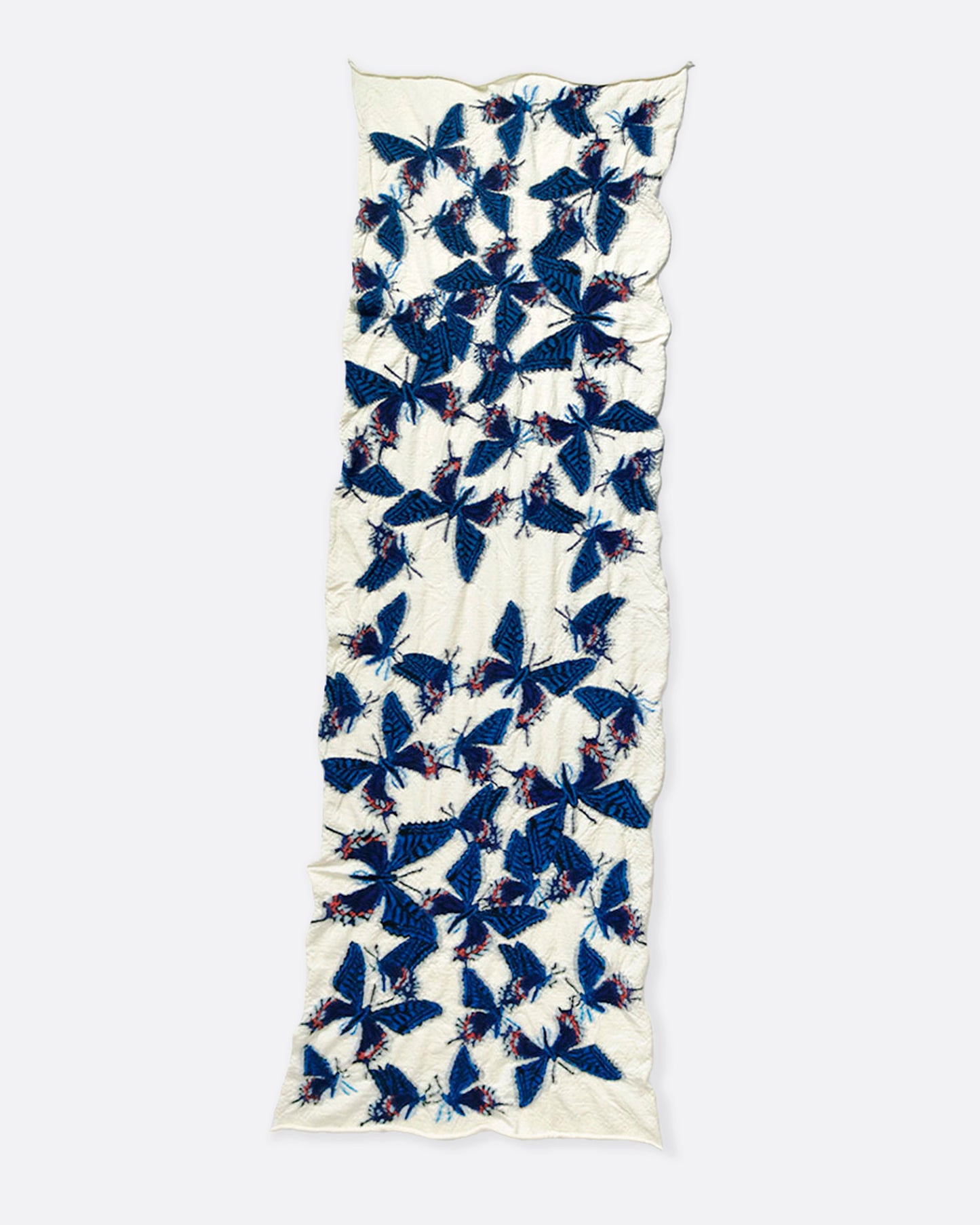 A white compressed wool scarf with blue butterflies all over it, shown lying flat.