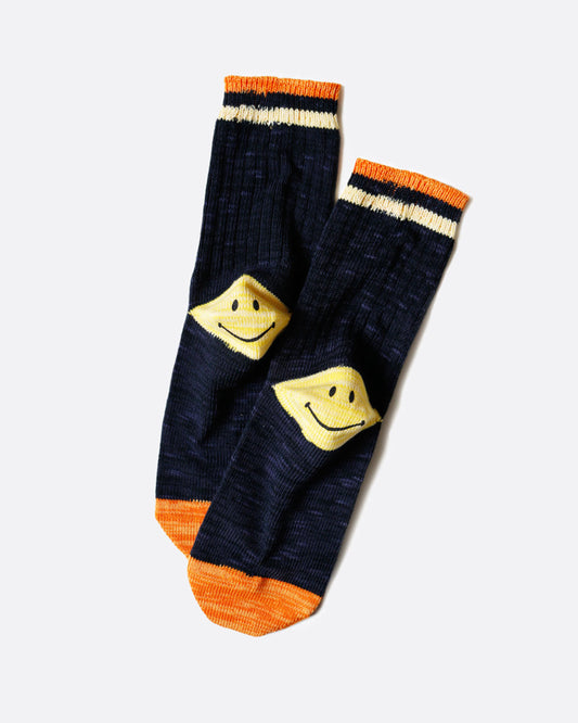 A pair of navy socks with orange stripes at the ankle and orange toes. Each heel has a yellow Kapital smiley face. Shown lying flat from the back.