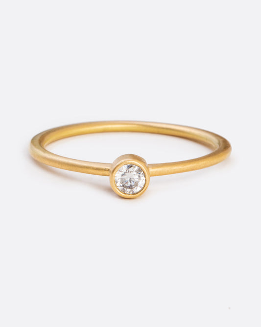 A yellow gold ring with a bezel set round diamond. Shown from the front.