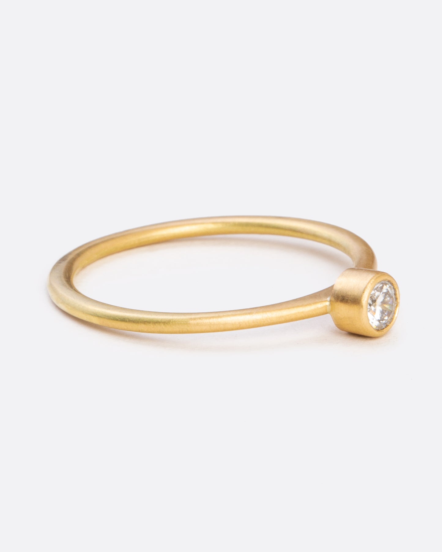 A yellow gold ring with a bezel set round diamond. Shown from the side.