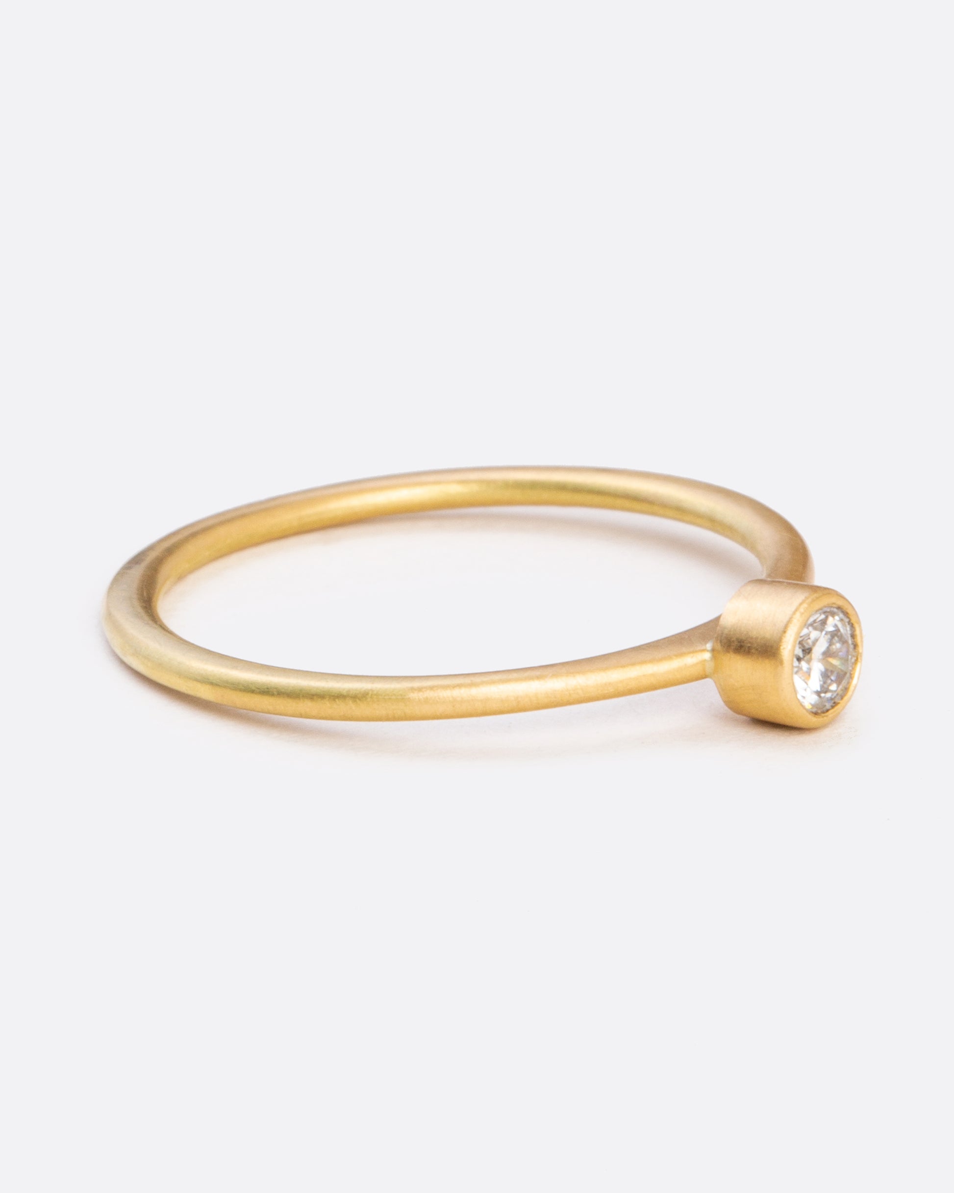 A yellow gold ring with a bezel set round diamond. Shown from the side.