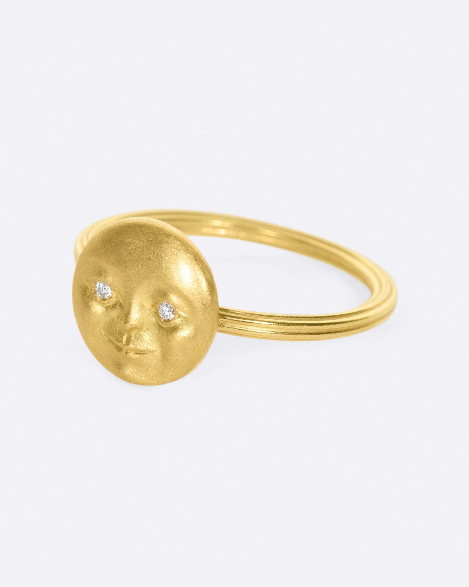 A yellow gold ring with a round moon face with diamond eyes. Shown from the side.