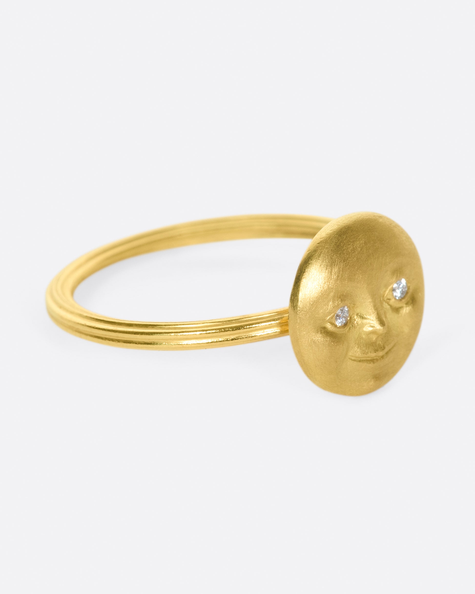 A yellow gold ring with a round moon face with diamond eyes. Shown from the side.