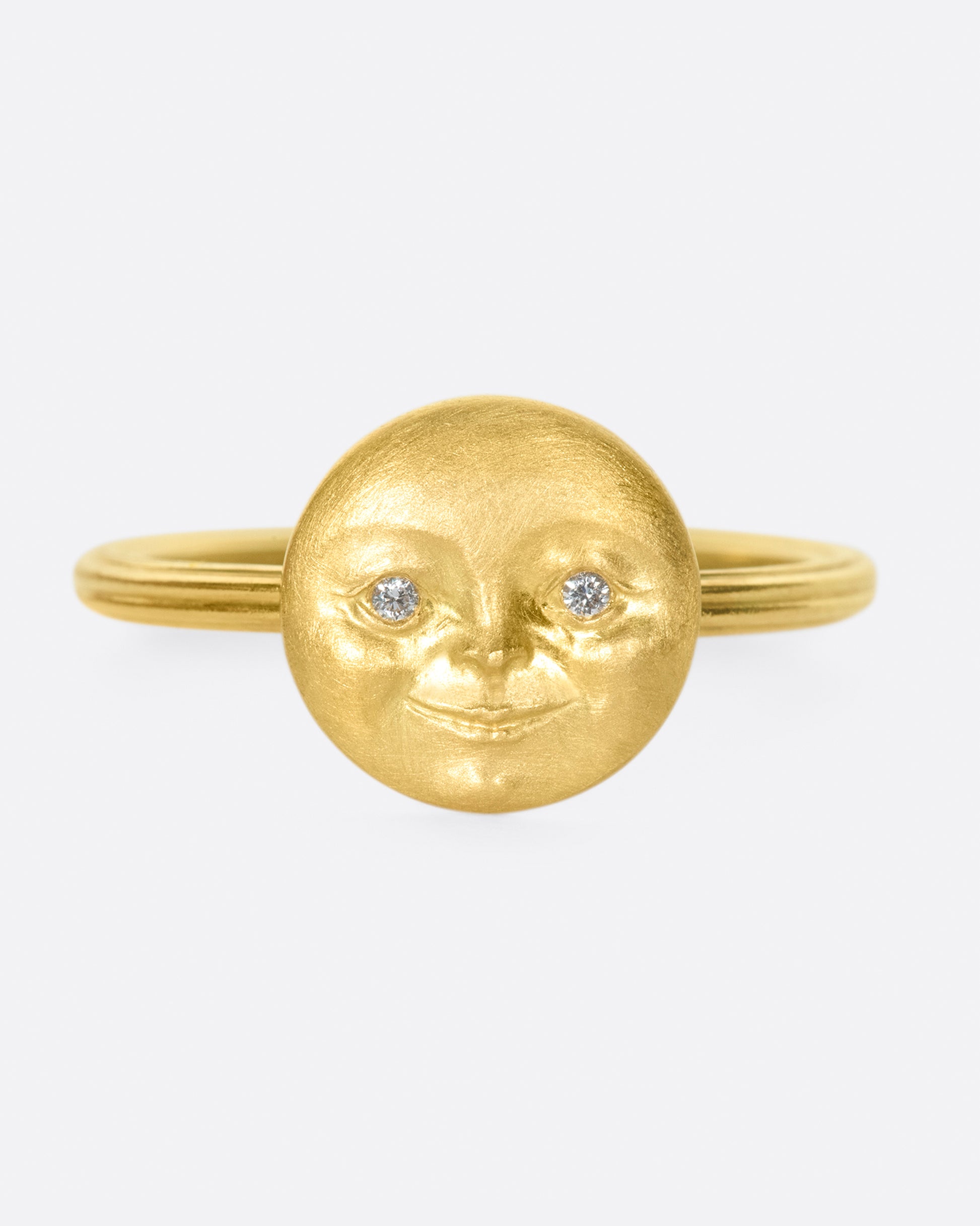 A yellow gold ring with a round moon face with diamond eyes. Shown from the front.