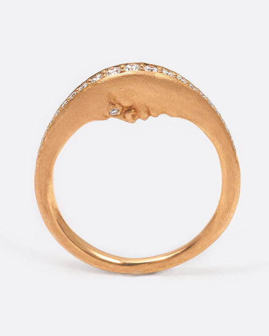 A rose gold crescent moon ring with a diamond eyed face. The top edge has a row of diamonds. Shown standing up from the side.