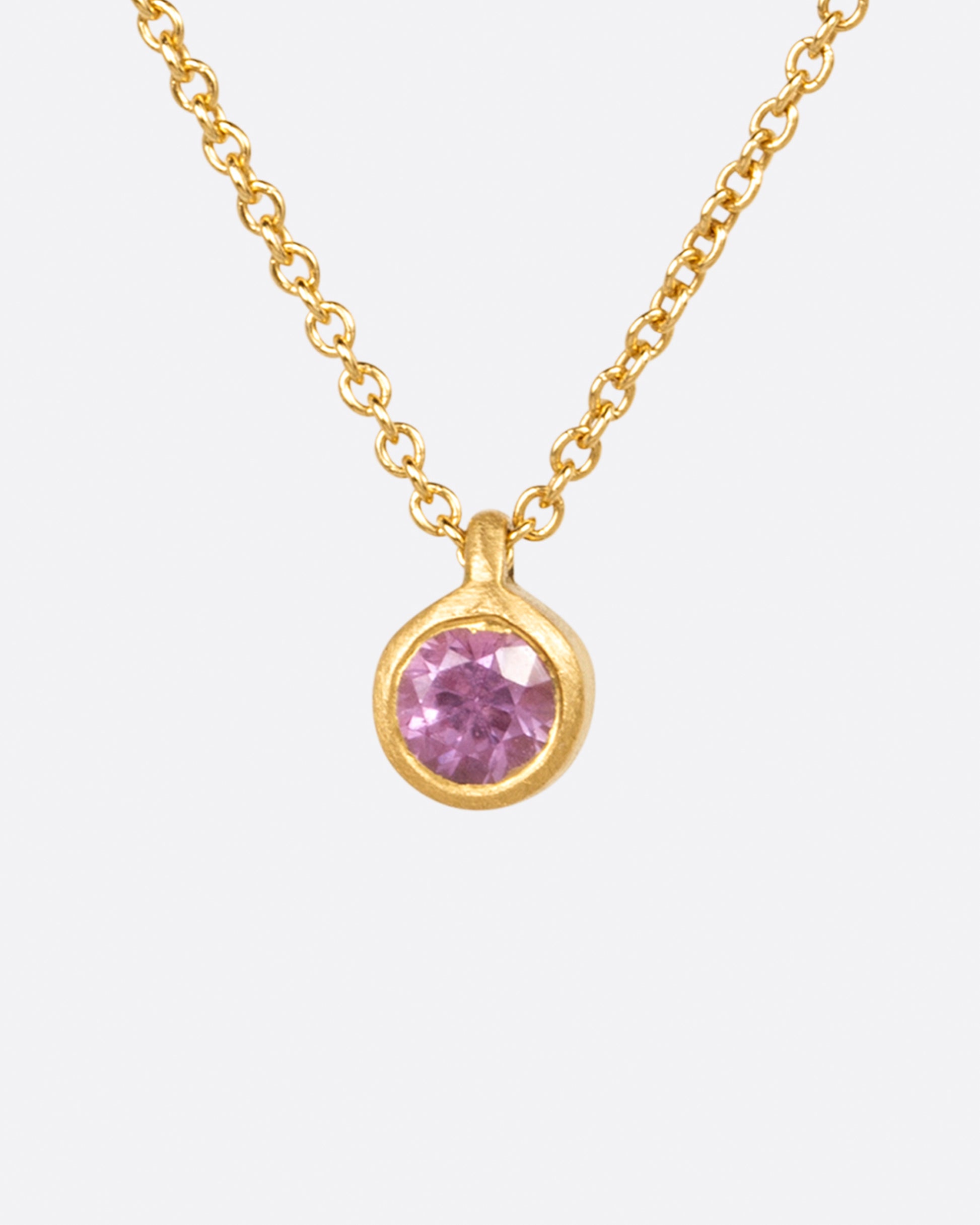 A rosy pink sapphire pendant set in a matte yellow gold bezel