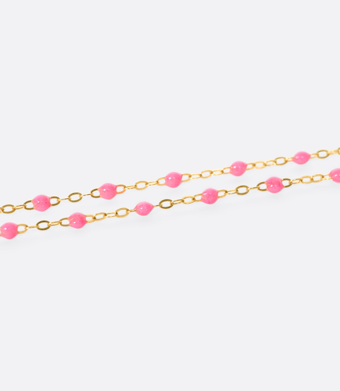 A close up view of a yellow gold cable chain necklace with pink resin droplets. Shown from the side.