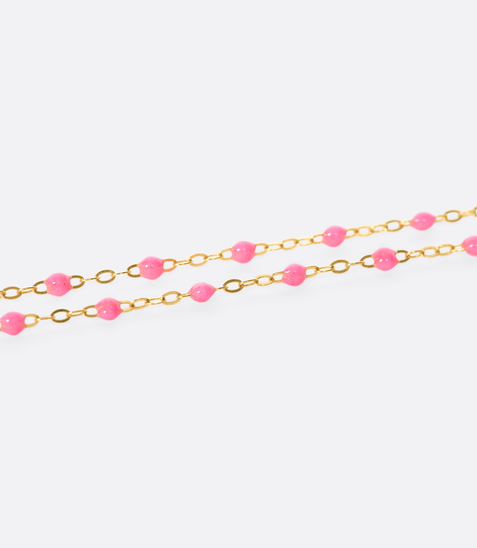 A close up view of a yellow gold cable chain necklace with pink resin droplets. Shown from the side.