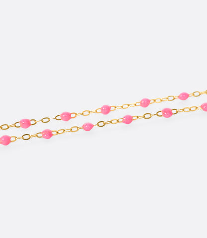 A close up view of a yellow gold cable chain necklace with pink resin droplets. Shown from the side.