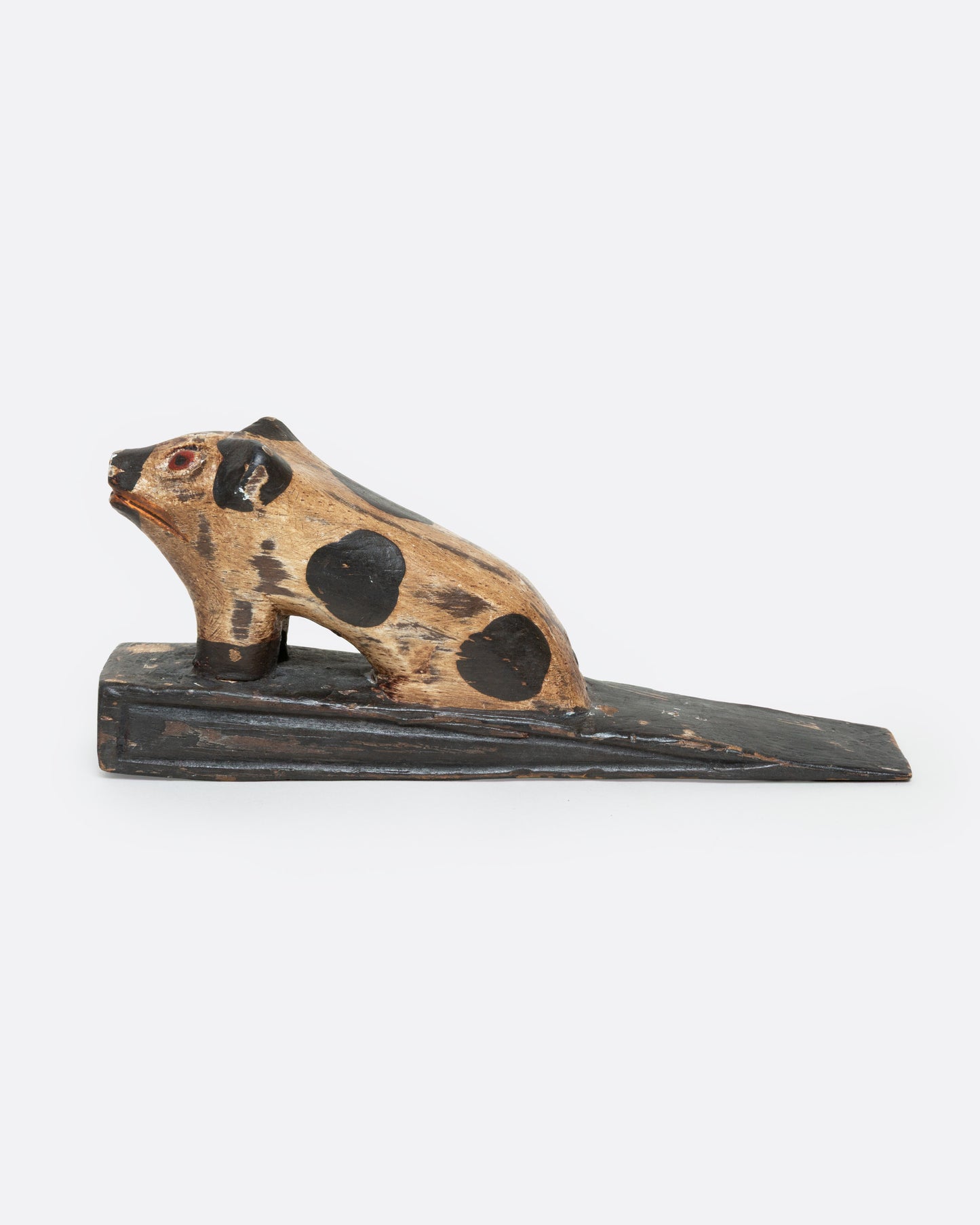 A hand carved wooden door stop with a spotted pig, shown from the side.