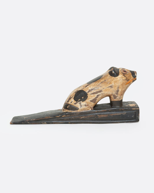 A hand carved wooden door stop with a spotted pig, shown from the side.