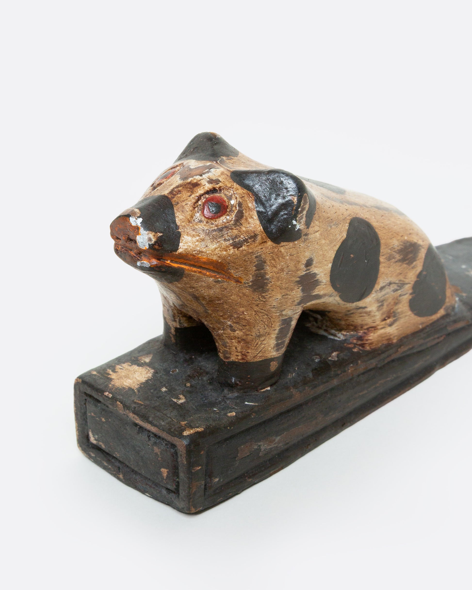 A hand carved wooden door stop with a spotted pig, shown from the side.