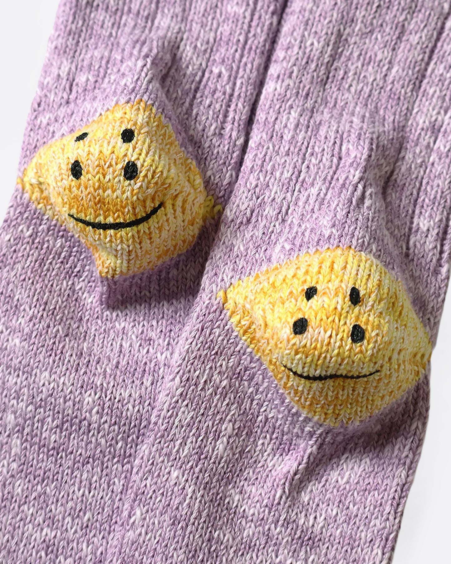 A pair of purple ribbed cotton socks with double-eyed smiley faces on each heel, shown from the bottom close up.
