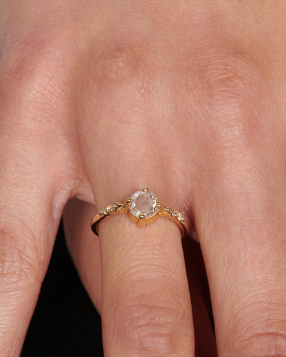 A yellow gold ring with a prong set rose cut diamond at the center and two diamonds on either side, shown from the front on a person.