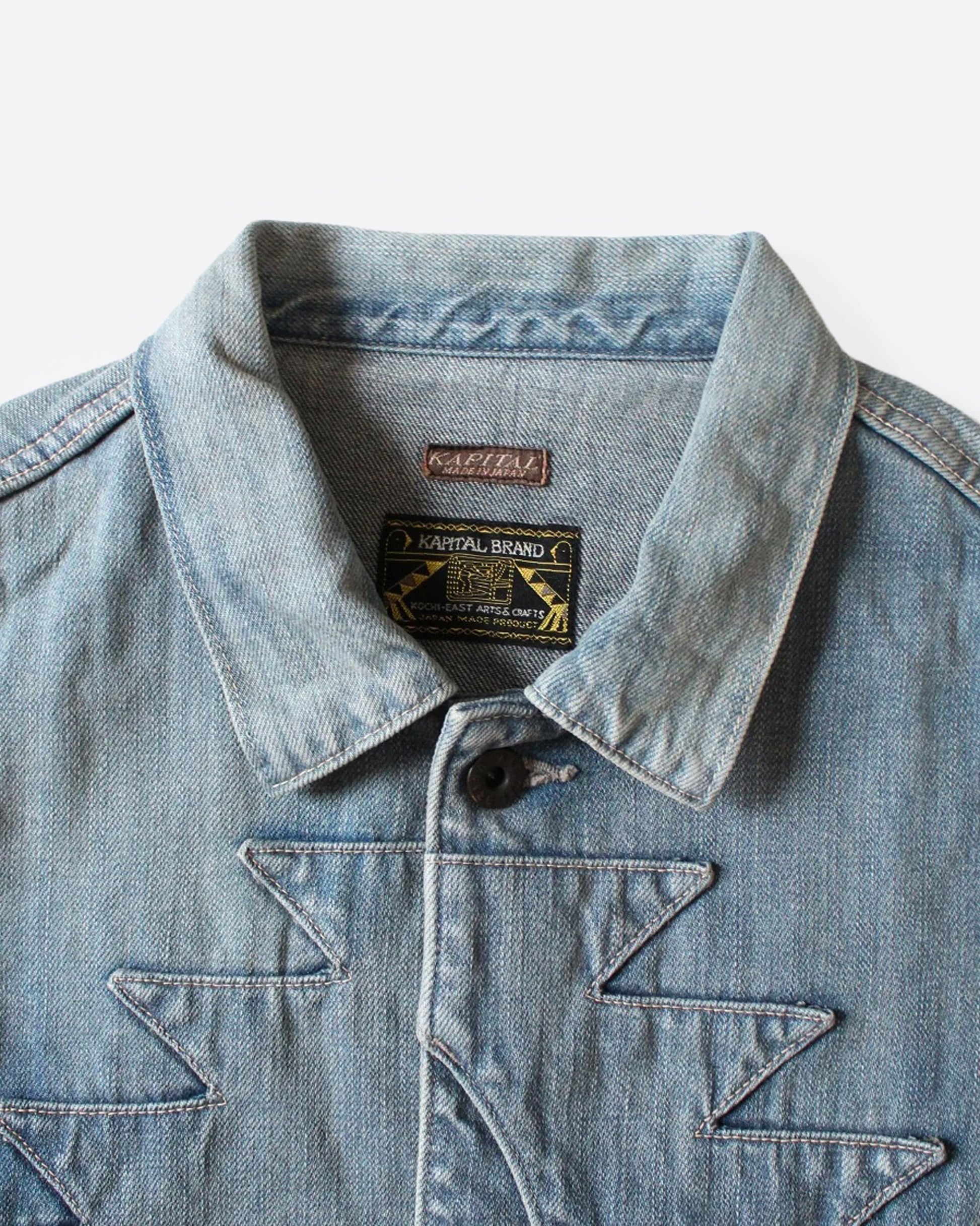 A close up of a light blue denim jacket with Chimayo-inspired embroidery across the chest and at each elbow, button closures, and functional back cinch. 