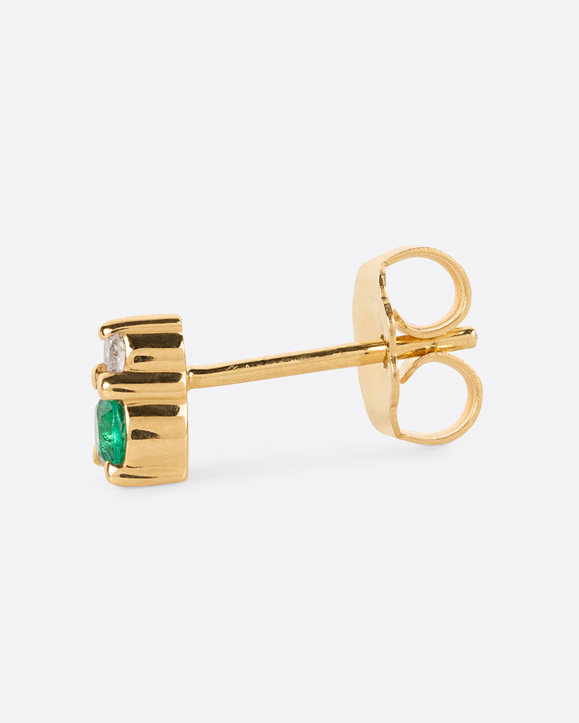 A yellow gold stud earring with a diamond on top and an emerald on the bottom. Shown from the side.