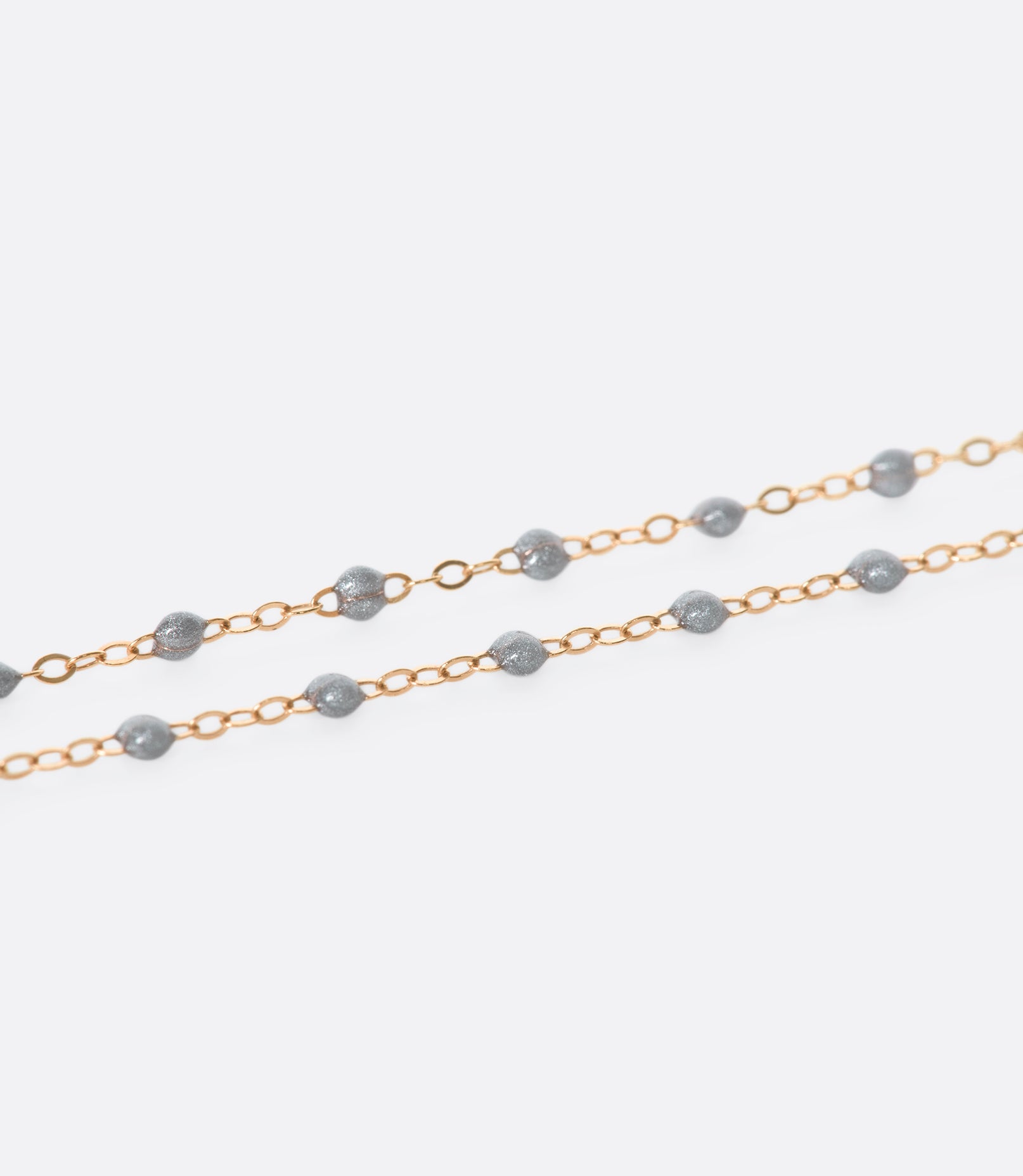 A close up view of a yellow gold cable chain necklace with silver resin droplets. Shown from the side.