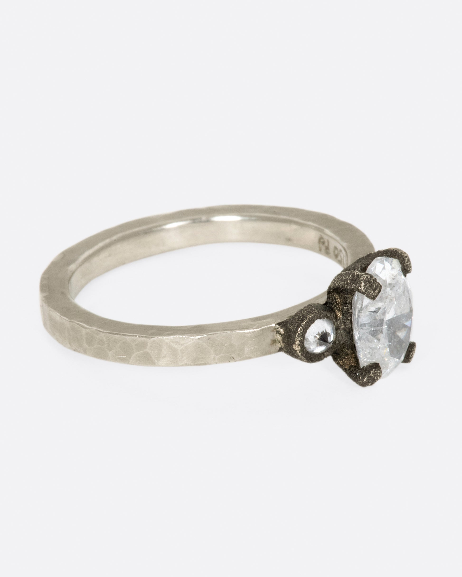 A hammered palladium band with three diamonds set in darkened white gold settings; one larger oval diamond flanked by two inverted round diamonds.