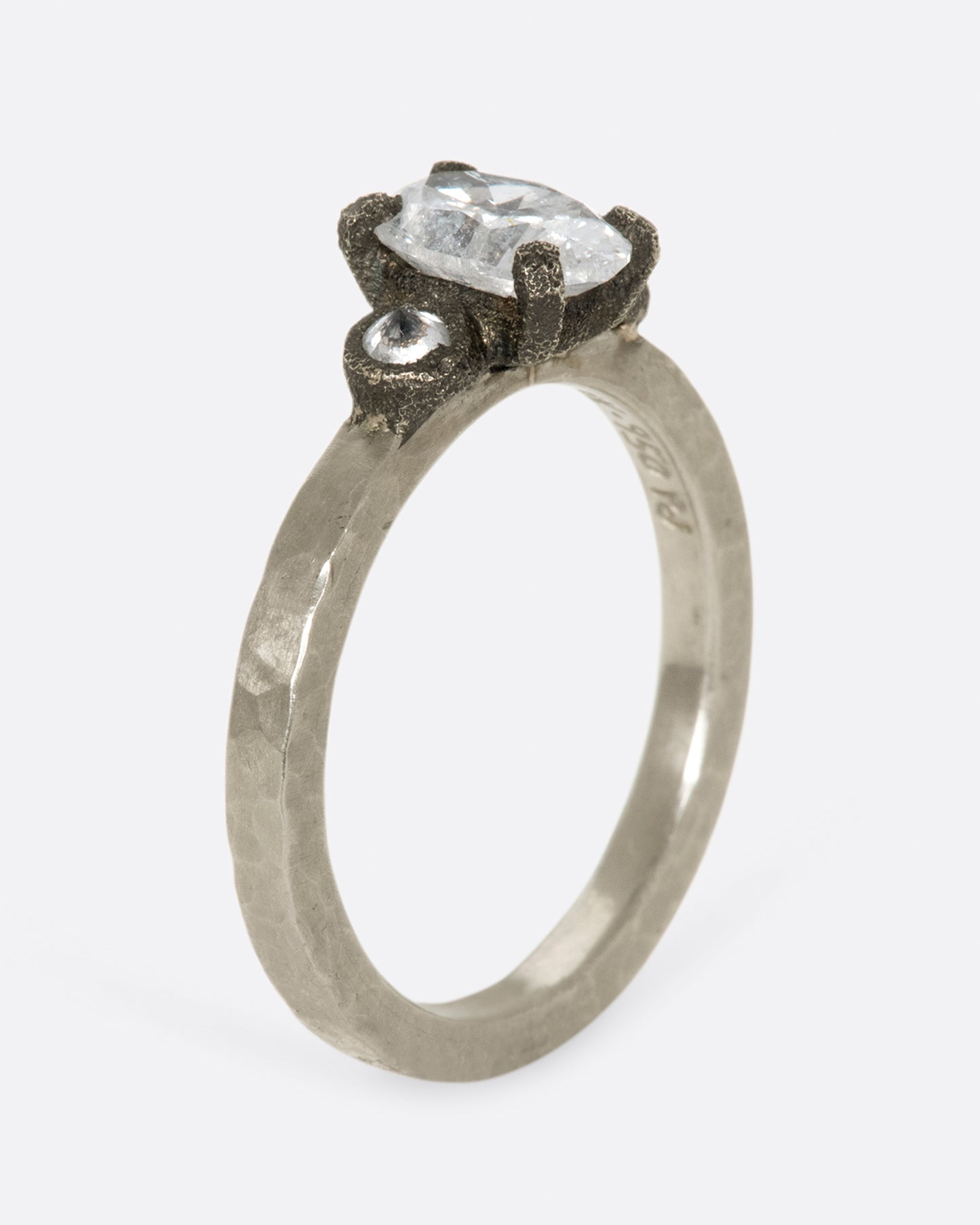 A hammered palladium band with three diamonds set in darkened white gold settings; one larger oval diamond flanked by two inverted round diamonds.