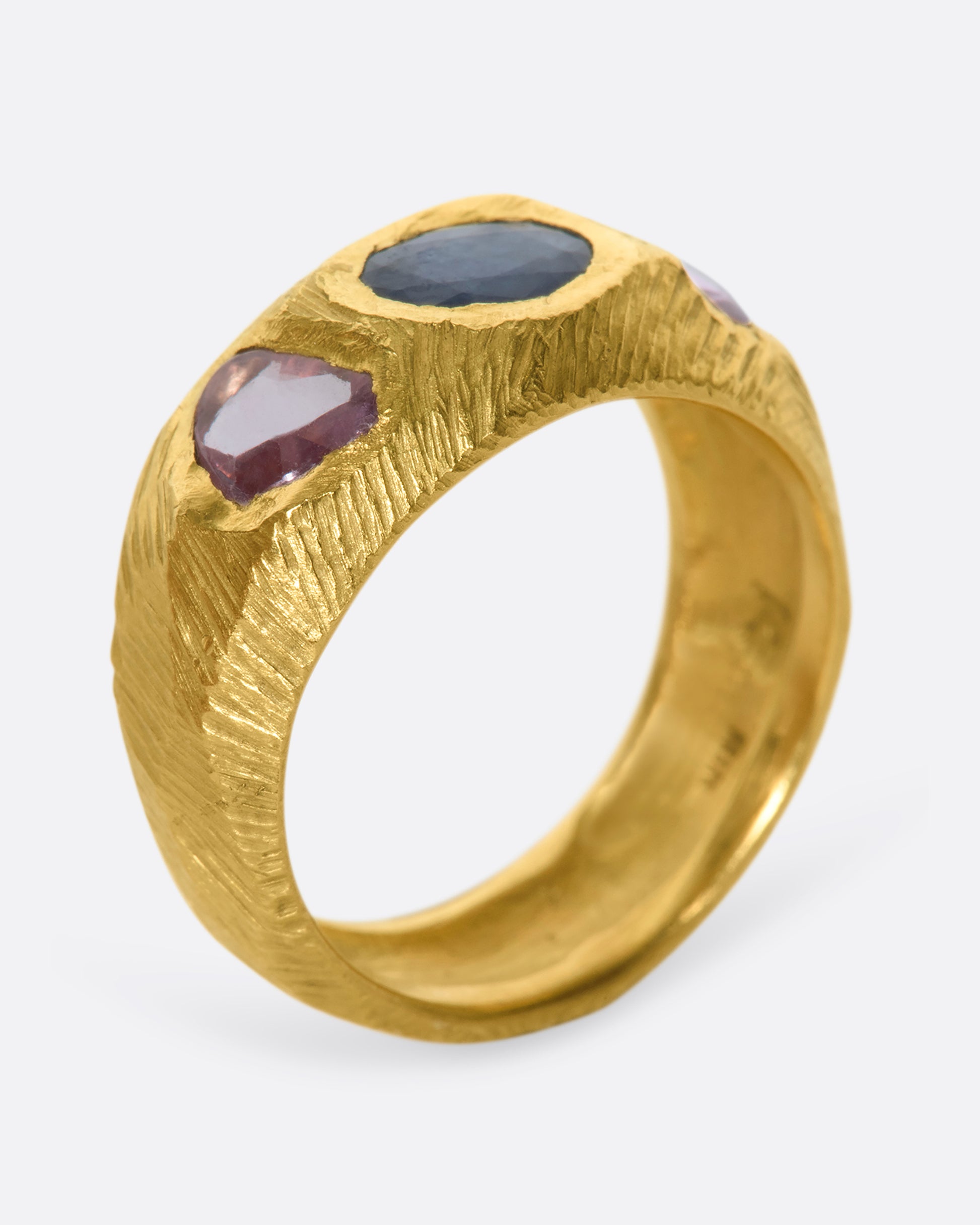 This hand carved 18k gold band is inlaid with an oval blue sapphire, flanked by beautiful pink sapphires