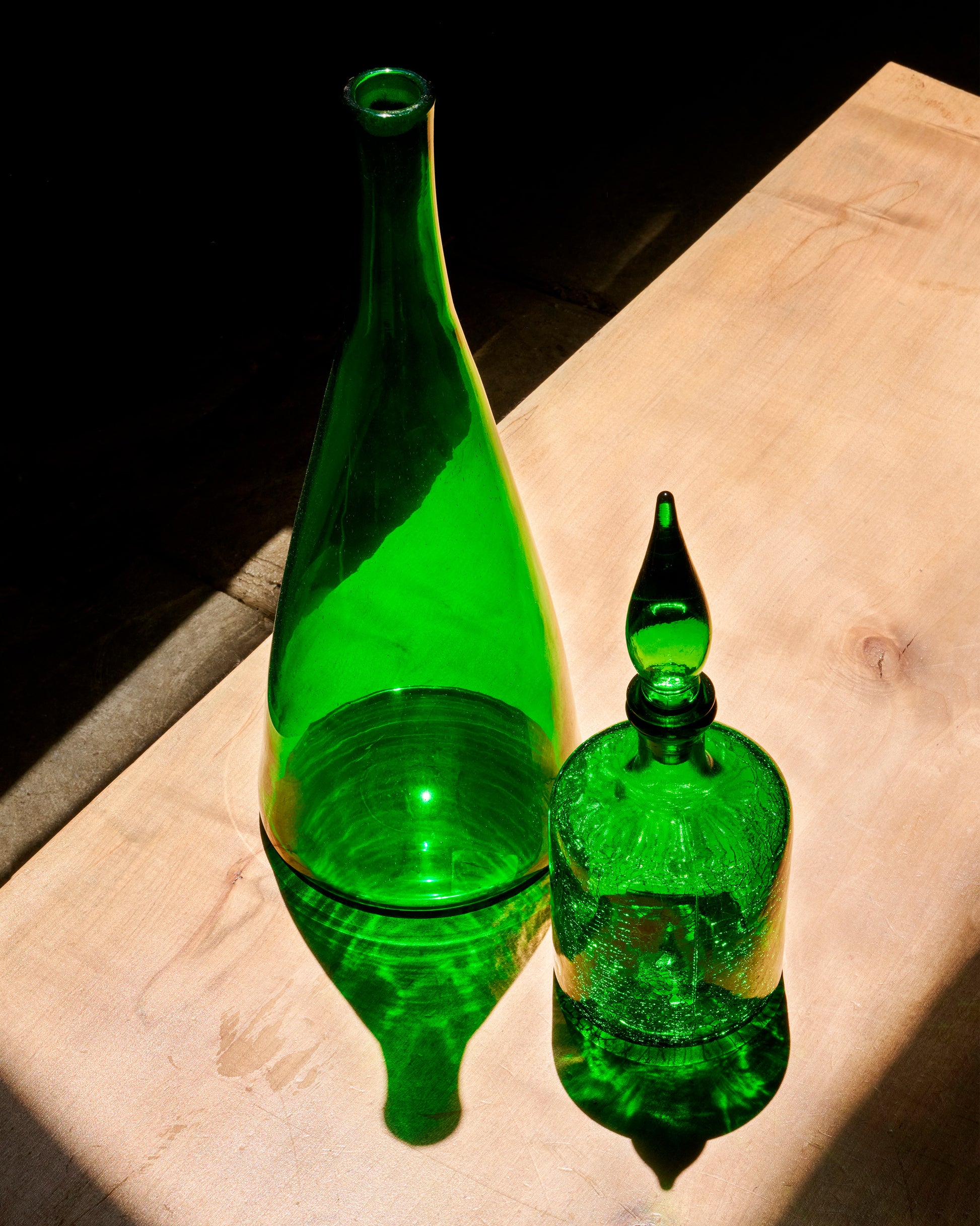 Two green glass bottles, shown from the front in a sunny patch of light.