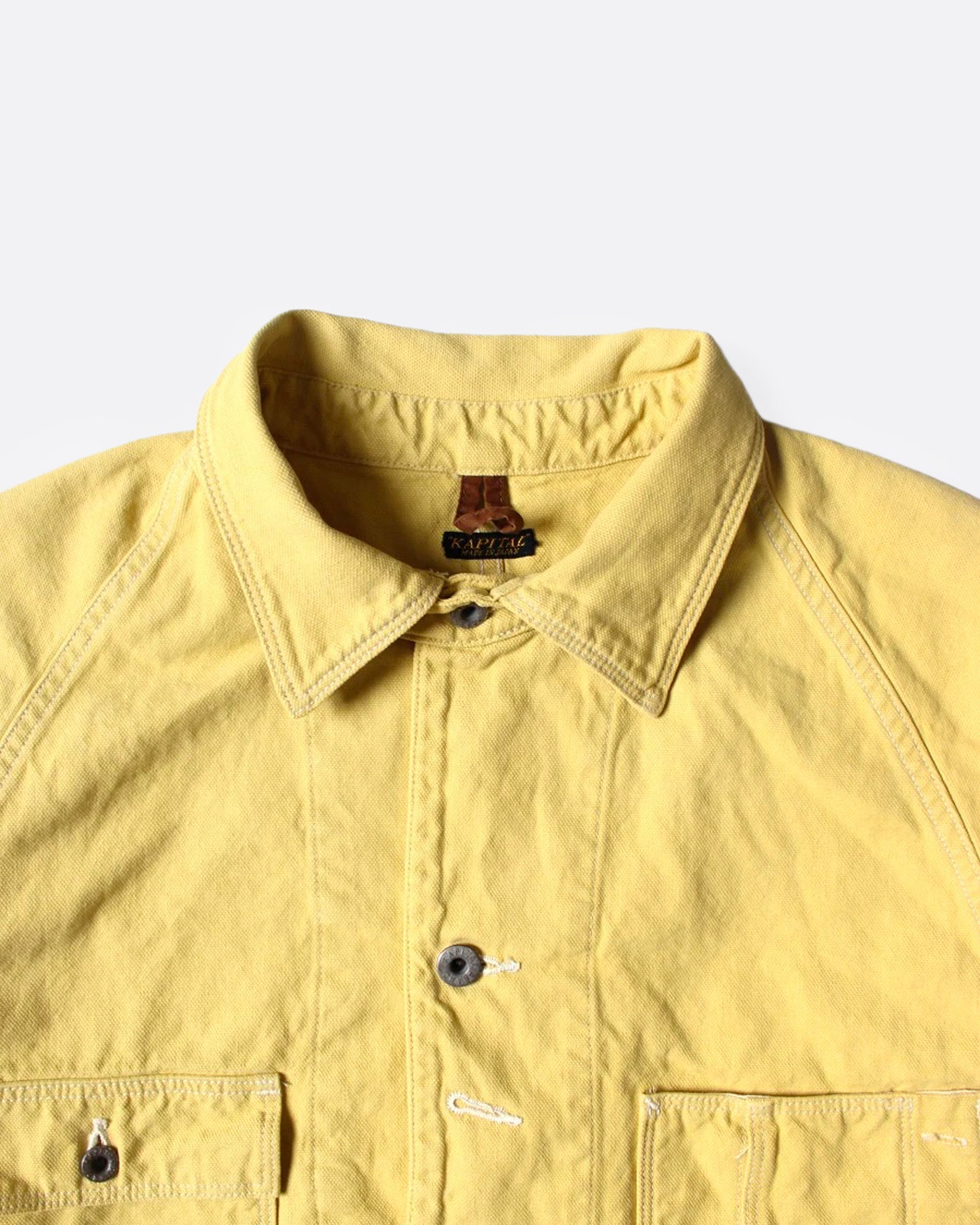A close uup of a A yellow canvas chore coat, shown from the front.