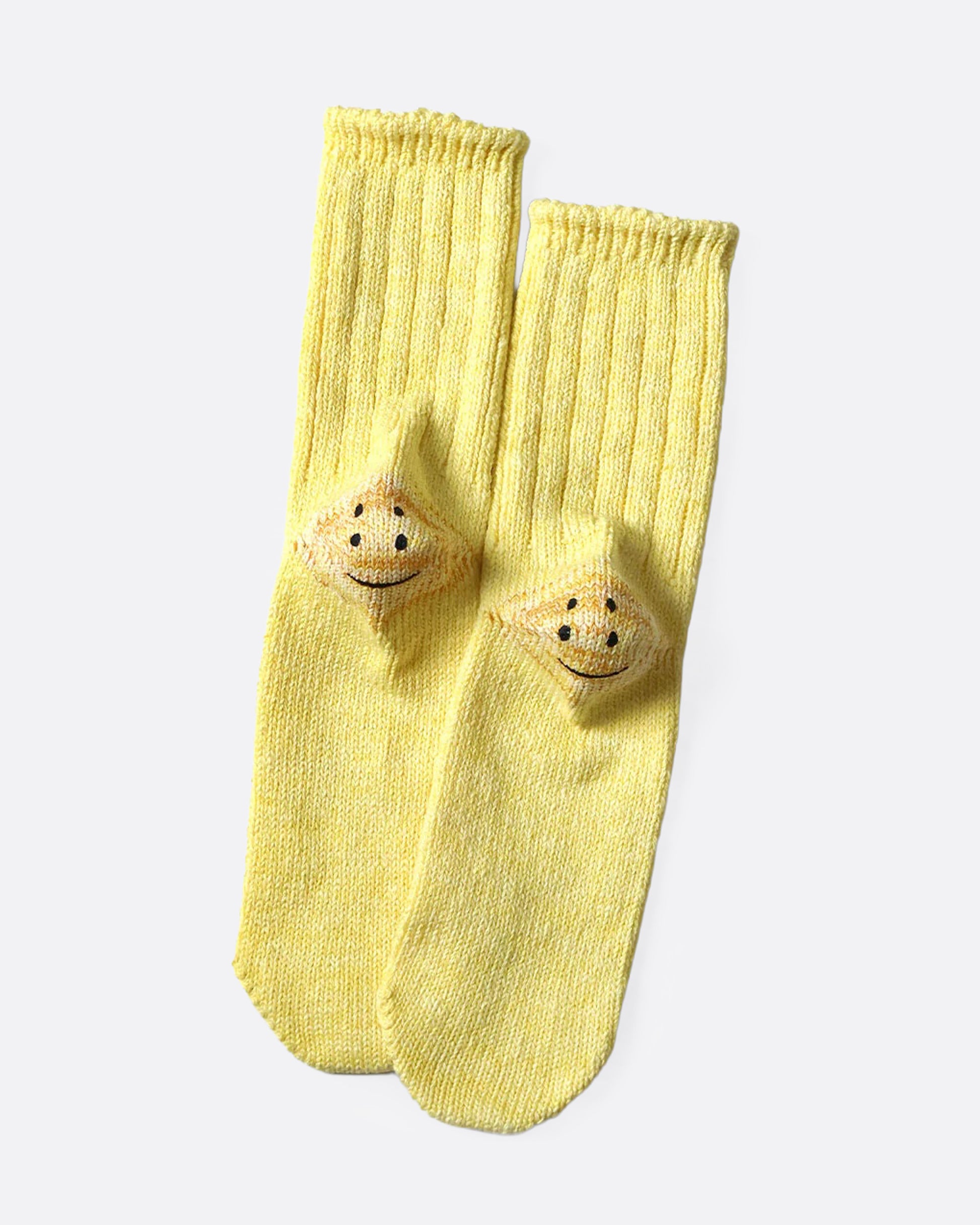 A pair of yellow ribbed cotton socks with double-eyed smiley faces on each heel, shown from the bottom.