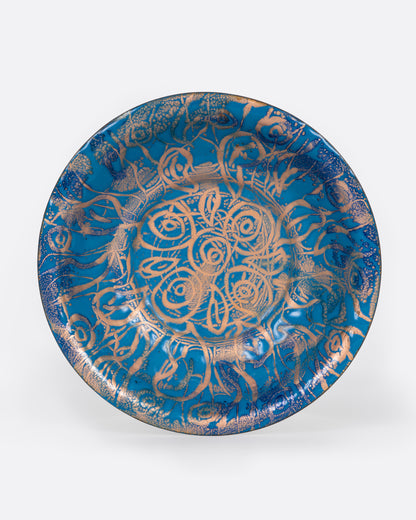 A blue enamel plate with a network of gold swirls, shown from the top.