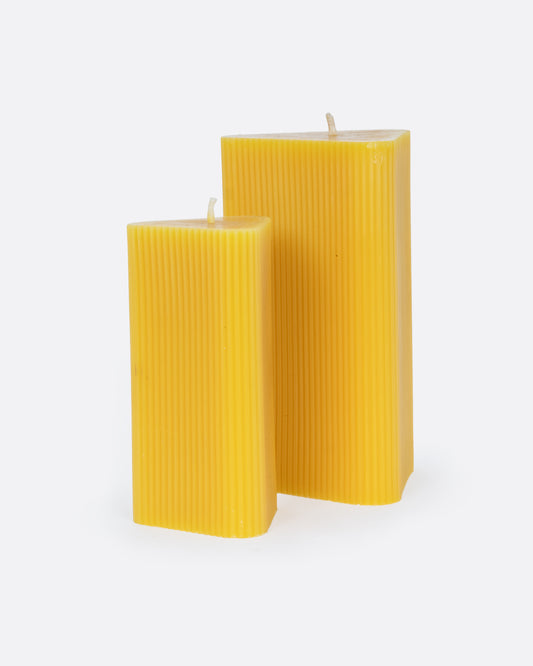 A pair of yellow beeswax fluted triangular candles- one small and one large. Shown from the side.
