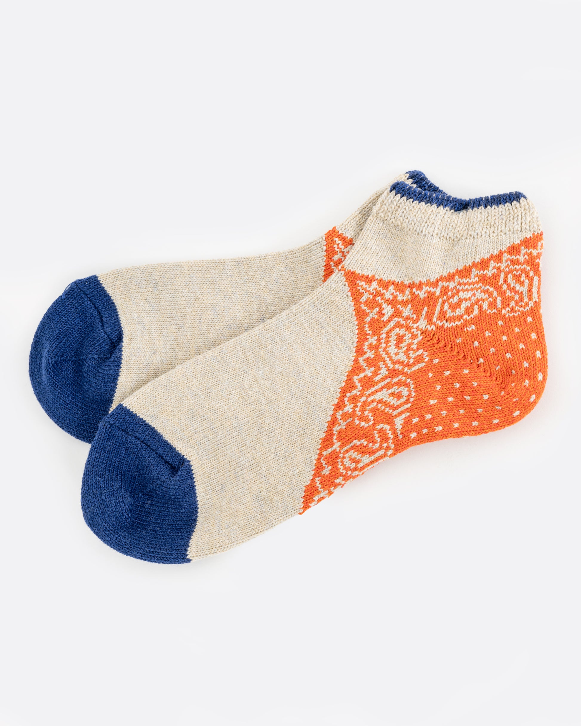 A pair of tan and blue ankle socks with an orange paisley bandana print heel. Shown lying flat from the side.