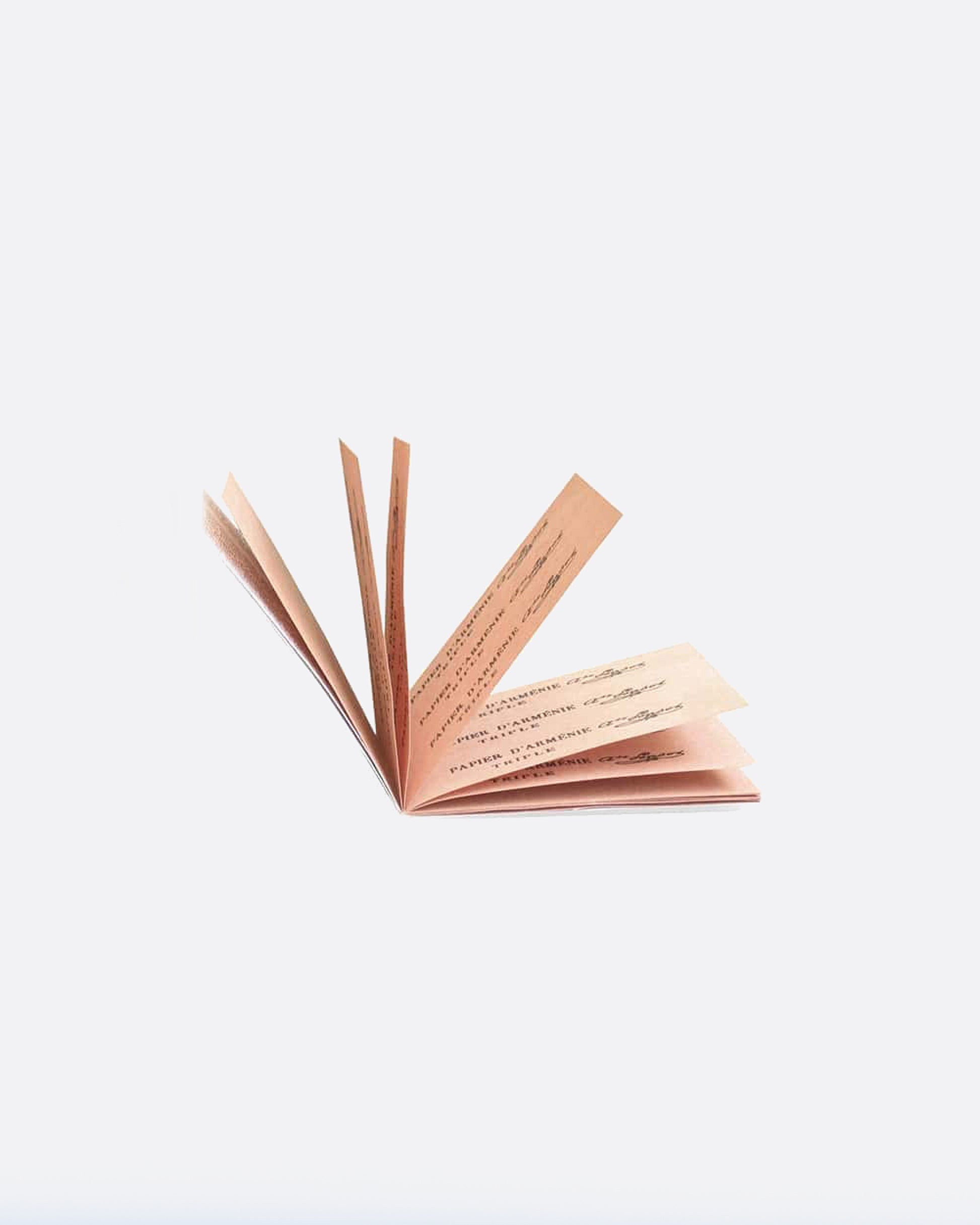 An open booklet of paper incense. Each page has strips of pink paper with writing on top. Shown lying flat from the front.