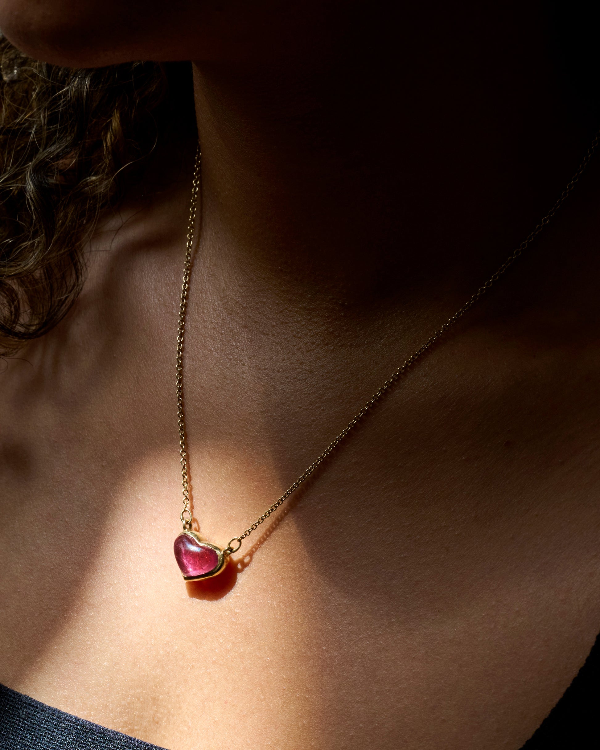 A yellow gold necklace with a rubellite heart shaped pendant, shown on a person.