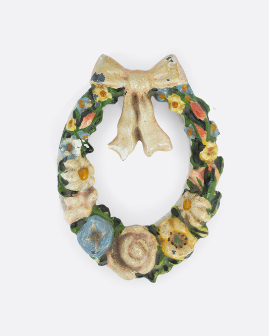 A cast  iron wreath door knocker with a bow and flowers. Shown from the front.