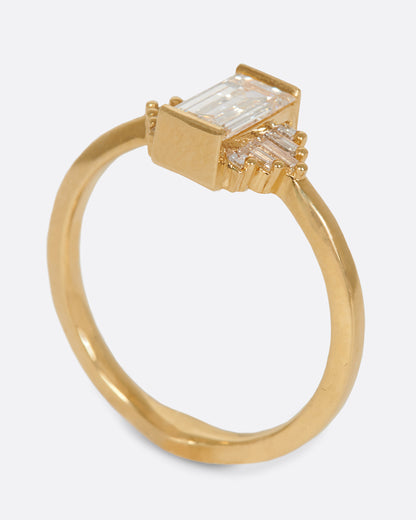 A large diamond baguette sits at the center of this ring, flanked by five additional baguettes on either side. Shown standing up from the side.