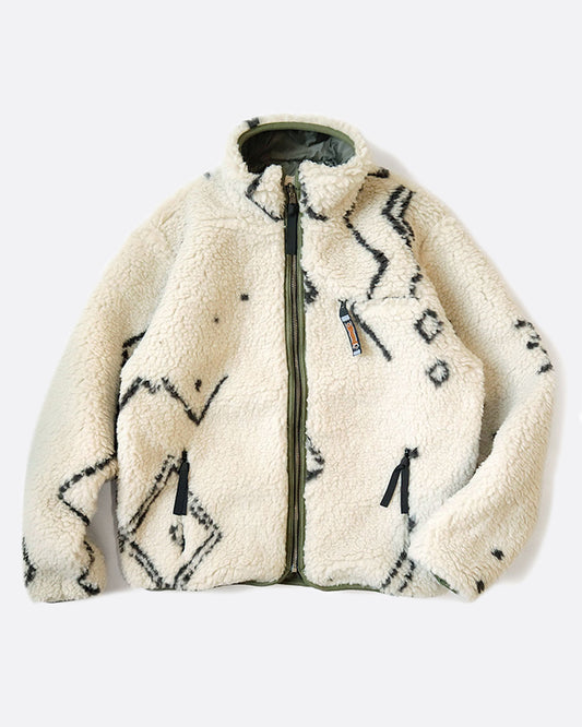 A reversible jacket with white Beni Ourain patterned fleece on one side and a green nylon shell on the other, shown lying flat on the fleece side from the front.