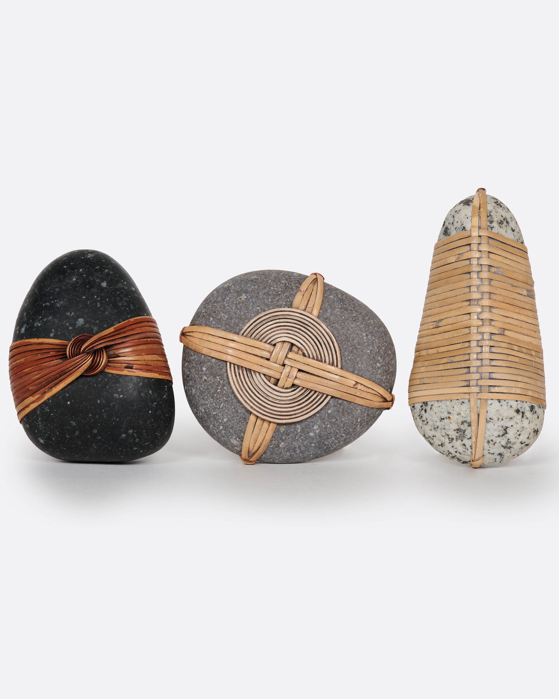 A group of three blessing stones, each wrapped and woven with grasses . Shown from the front standing up.