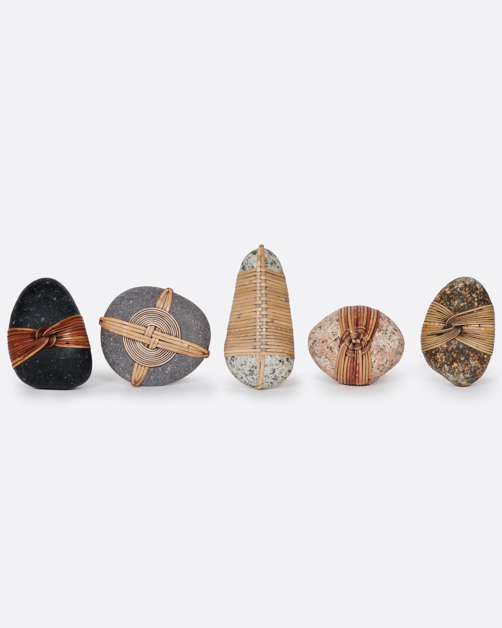 A group of five blessing stones, each wrapped and woven with grasses . Shown from the front standing up.