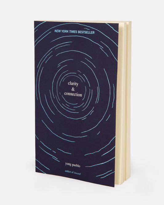 A book titled 'clarity & connection' by young pueblo with a navy blue cover with a light blue swirl pattern and white pages. Shown standing up from the front.
