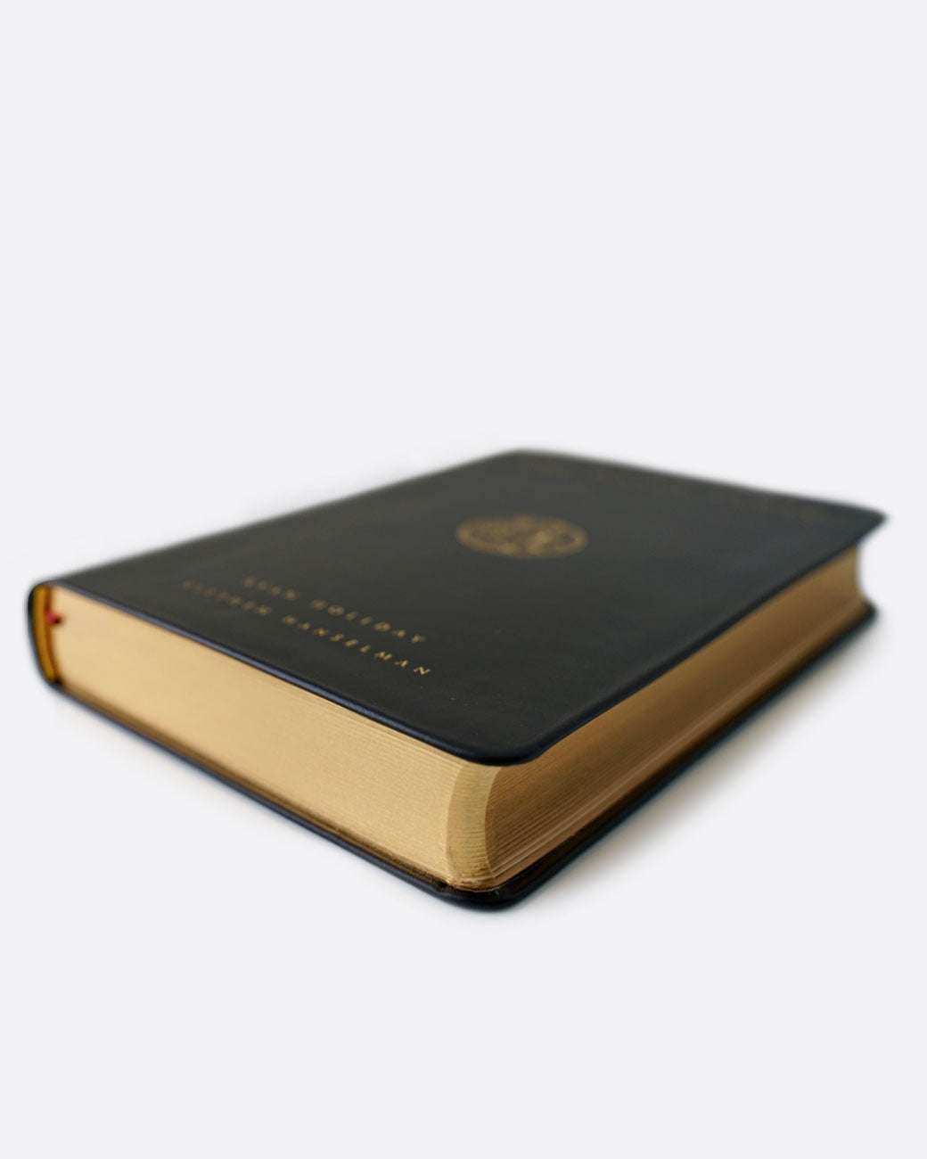 A black leather-bound book with gold pages. Shown at an angle from the side.