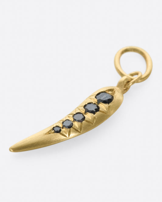 A yellow gold chili shaped charm with five graduated black diamonds. Shown laying flat.