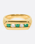 A yellow gold ring with a row of five channel set stones; three emeralds and two diamonds. Shown from the front.