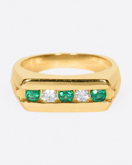A yellow gold ring with a row of five channel set stones; three emeralds and two diamonds. Shown from the front.