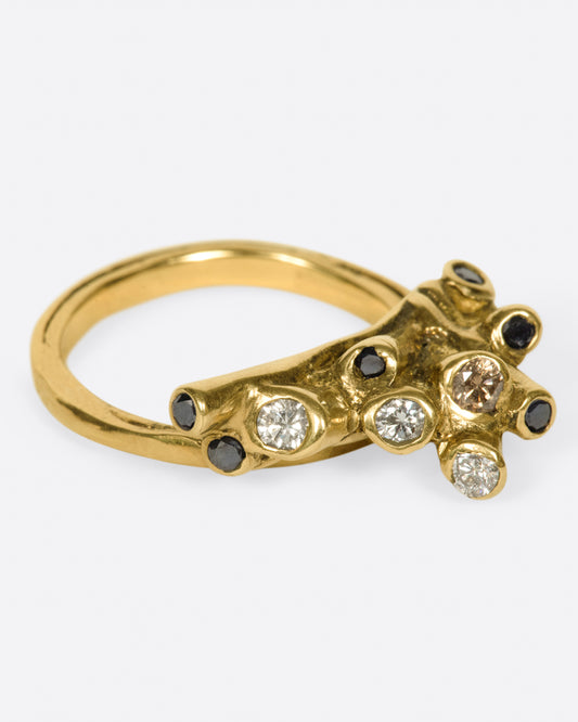 A ring with white, black, and cognac diamonds set in an anemone-like cluster. Shown from the side.