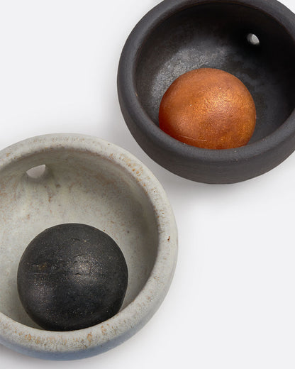 Two stoneware soap dishes- one black and one white with drainage spouts. Shown from the top each with a round soap in.