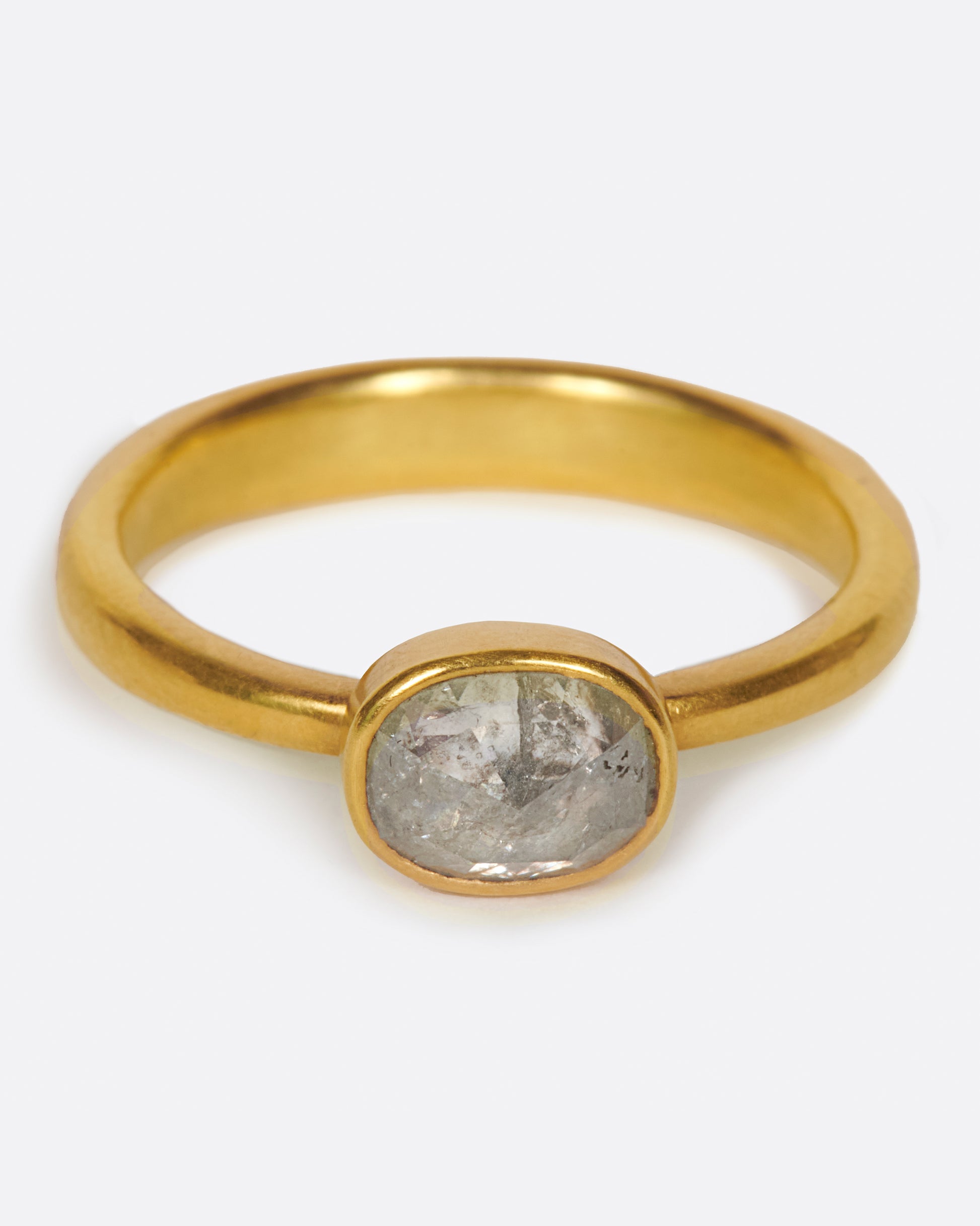 A pale grey, rose cut, oval diamond. Set horizontally on a simple, yellow gold band. Shown from the front.