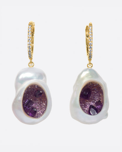 A pair of dangle earrings with carved out pearls lined with amethysts. Each earring is topped with  yellow gold ear hook with pave diamonds. Shown from the front.