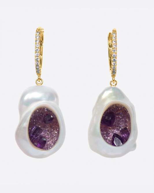 A pair of dangle earrings with carved out pearls lined with amethysts. Each earring is topped with  yellow gold ear hook with pave diamonds. Shown from the front.