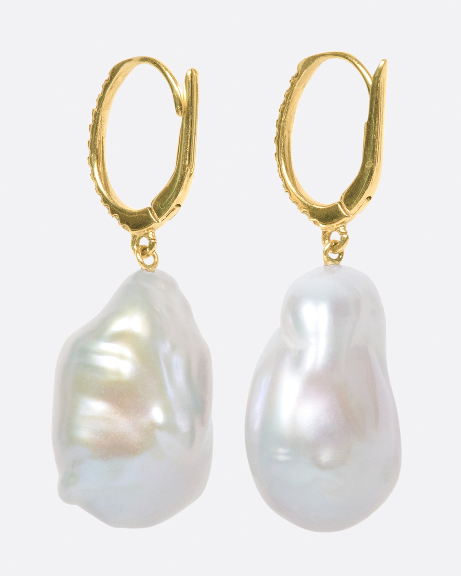 A pair of dangle earrings with carved out pearls lined with amethysts. Each earring is topped with  yellow gold ear hook with pave diamonds. Shown from the back.